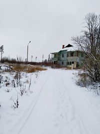 Snow covered road by buildings against sky