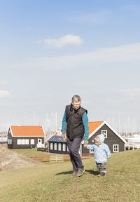 Grandfather and granddaughter walking on field against sky