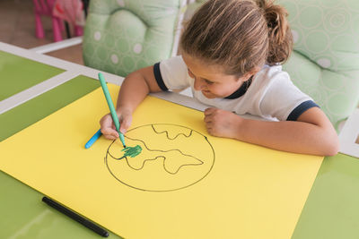 Smiling blond girl coloring earth sketch at home