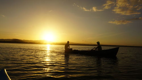 Silhouette people in sea against sky during sunset