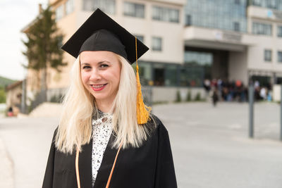 Portrait of woman wearing graduation gown standing in city