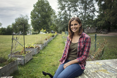 Portrait of smiling mid adult woman sitting on wood in vegetable garden