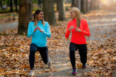 Woman exercising in public park with personal trainer in the fall.