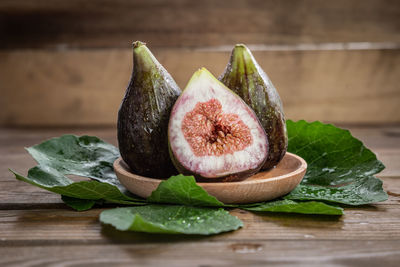 Fresh figs on wooden plate with fig leaves on wooden background.