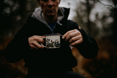 Midsection of man holding cup in forest
