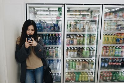 Young woman using phone by refrigerator at market