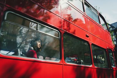 Low angle view of young woman looking through bus window during sunny day