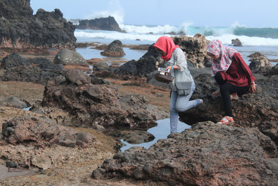 People standing on rock by sea against sky