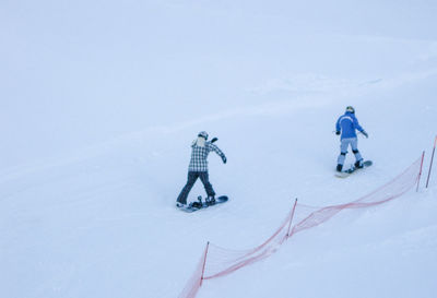 Rear view of people snowboarding on snowy field