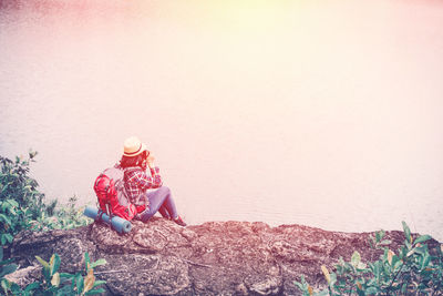 High angle view of young woman with backpack looking at lake while sitting on rock