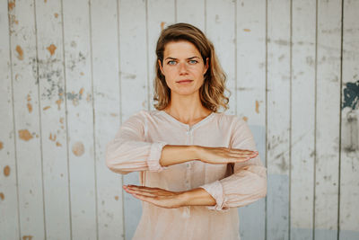Portrait of woman gesturing equal sign while standing against wall