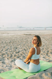 A beautiful girl is sitting on the seashore in the lotus position and resting after yoga