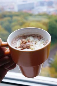 Cropped hand holding coffee against window