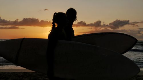 Silhouette people on shore against sky during sunset