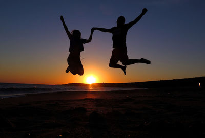 Silhouette couple jumping on shore at beach against clear sky during sunset