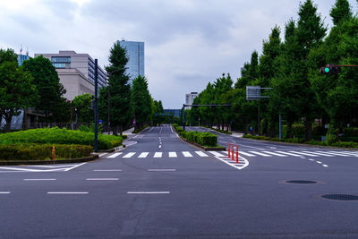 Road amidst trees and city against sky