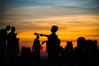 Silhouette people against orange sky