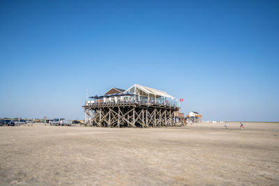 Traditional windmill on beach against clear blue sky