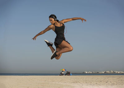 Young woman dancing at beach against clear sky