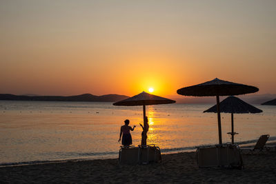 Silhouette people on beach against sky during sunset