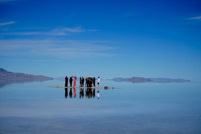 People standing amidst calm lake at bonneville salt flats against sky