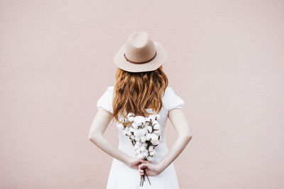 Rear view of woman wearing hat standing against white wall