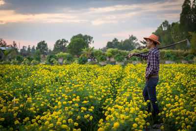 Woman standing on yellow flowers on field against sky