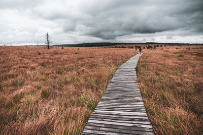 Boardwalk leading towards field against sky