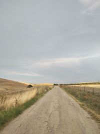 Dirt road amidst field against sky