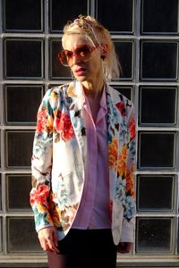 Portrait of young woman wearing sunglasses standing against window