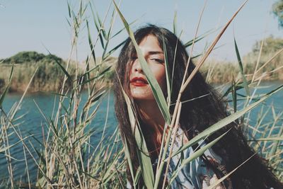 Portrait of young woman amidst plants against lake