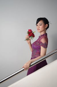 Side view of woman holding red roses while standing by railing