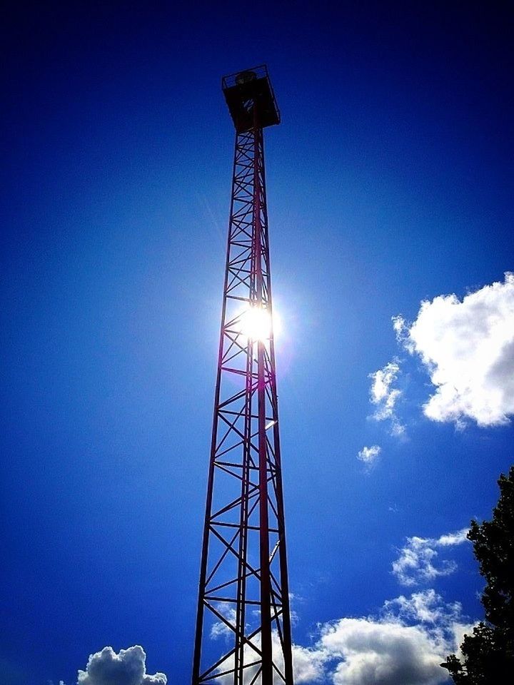 low angle view, blue, sky, tall - high, sun, tower, technology, silhouette, sunlight, electricity, clear sky, metal, sunbeam, fuel and power generation, lens flare, communications tower, built structure, outdoors, electricity pylon, no people