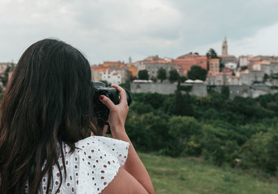 Rear view of young woman using using dslr camera, taking photos of hilltop town in labin, croatia