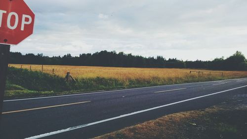 Road passing through field against cloudy sky