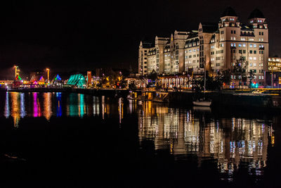 Illuminated buildings by river against sky at night