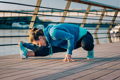 Young woman exercising on promenade by river during sunset