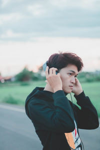 Man listening music while standing on land against sky