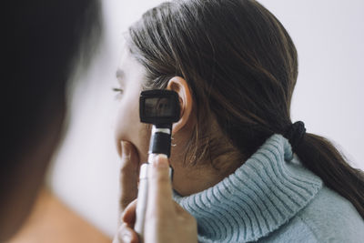 Doctor examining patient's ear using otoscope at hospital