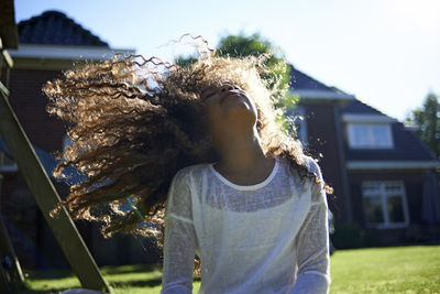 Happy girl shaking head while standing against house in backyard