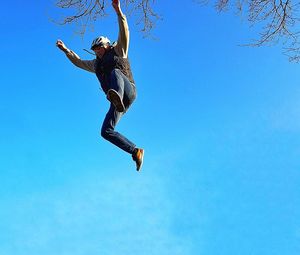 Low angle view of man jumping against clear blue sky