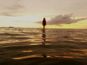 Rear view of woman standing on beach against sky during sunset