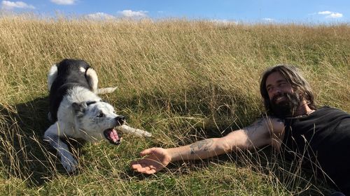 High angle view of mid adult man playing with dog while lying on grassy field