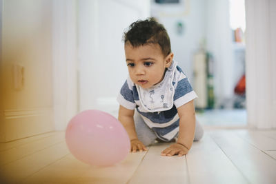 Toddler playing with balloon while crawling on floor at home