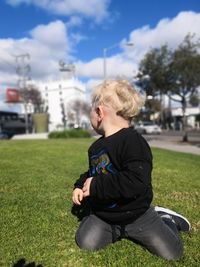 Boy on grass looking away against sky