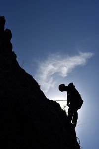 Low angle view of silhouette rock climber on mountain against blue sky