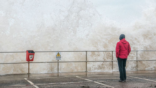 Rear view of person standing on promenade while wave splashing at sea shore