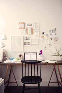 Chair and table with laptop computer against papers on wall at home