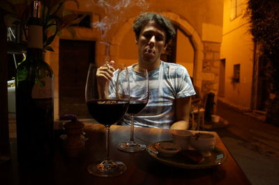 Man smoking cigarette while sitting by dining table in restaurant at night