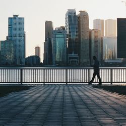 Full length side view of man walking by railing in city against sky